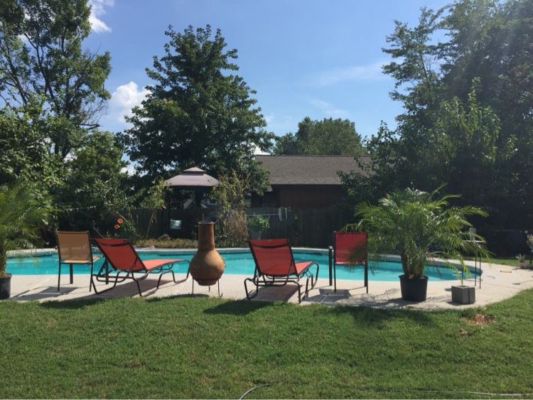 Backyard swimming pool with red lounge chairs and lawn